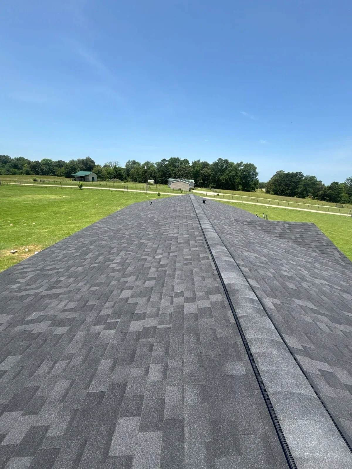Full ridge line of a fresh shingle roof replacement overlooking East Texas pastureland